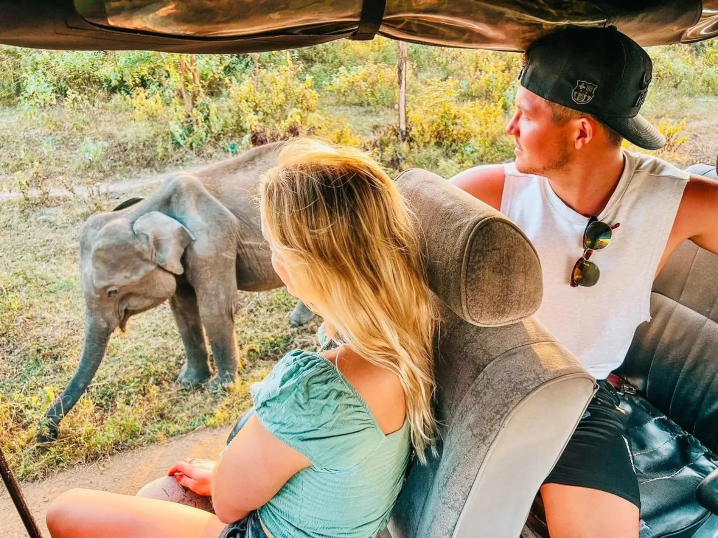 Two travellers watching an elephant beside their safari jeep