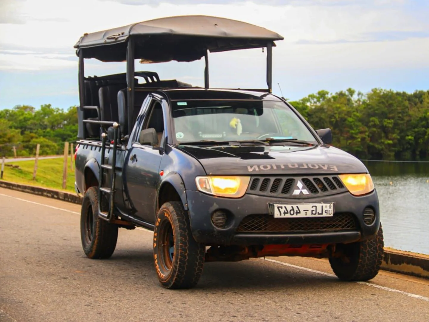 An open-sided safari jeep parked on a road beside a reservoir
